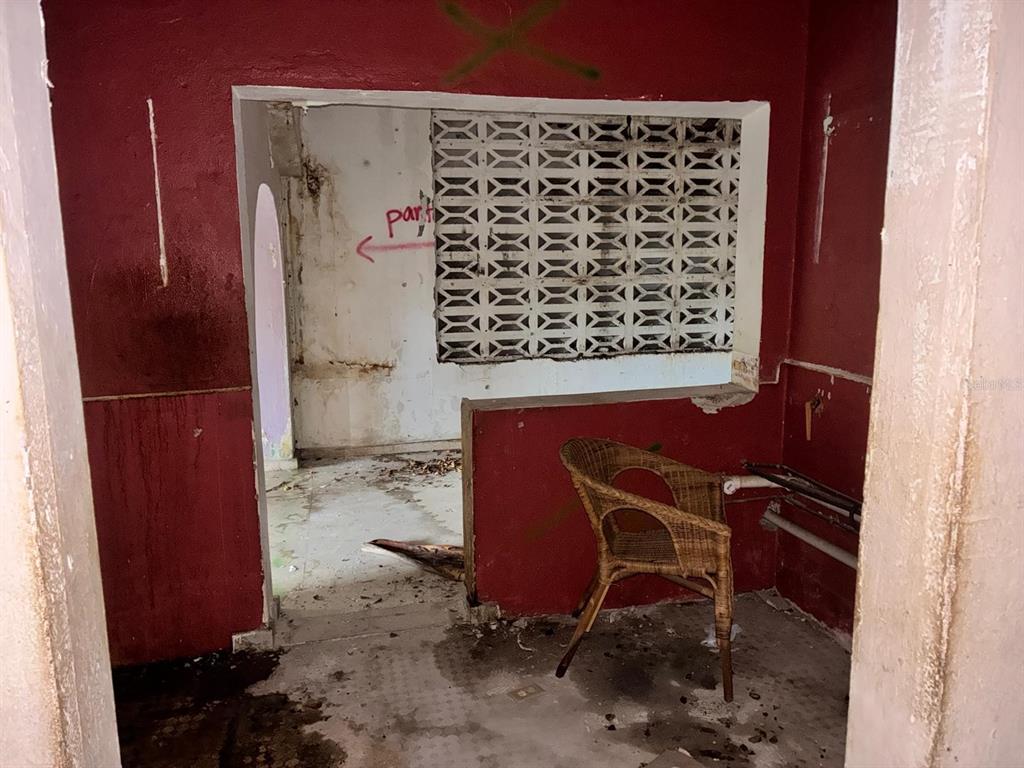An interior view of a dilapidated room with red walls, a wicker chair, and breeze blocks — 58 CALLE TENIENTE MATTA, SAN JUAN, PR