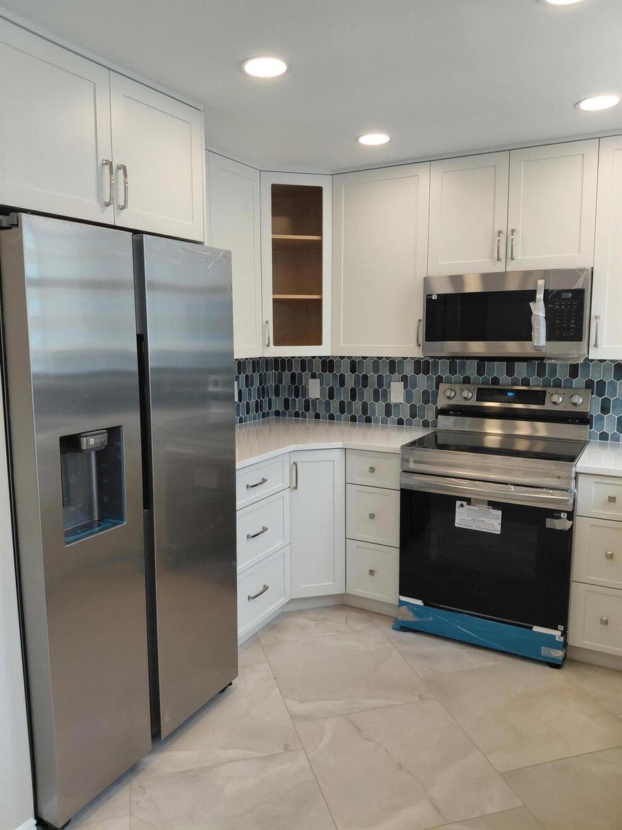 A kitchen features white cabinets, stainless steel appliances, and a blue hexagonal tile backsplash — 1010 S Ocean Boulevard # 1515, Pompano Beach FL 33062, POMPANO BEACH, FL