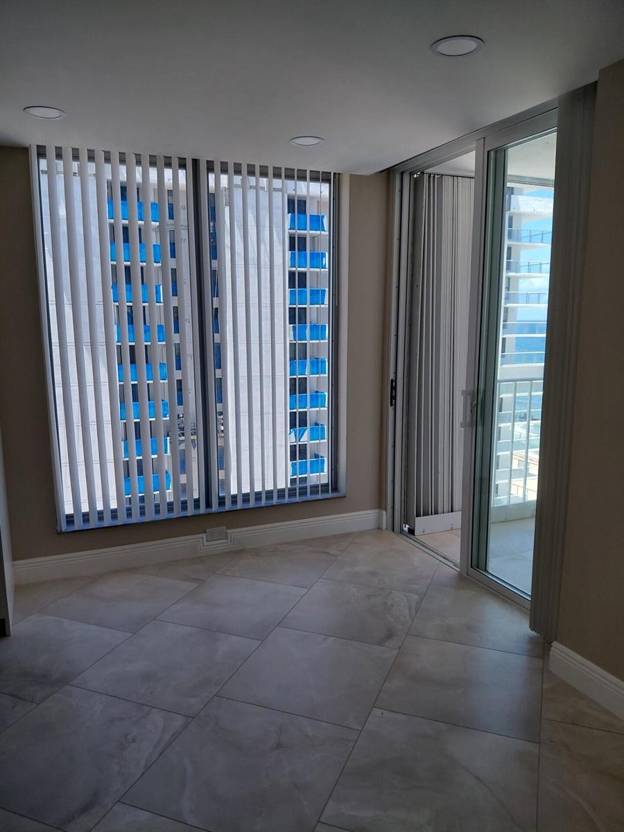 An empty room with large windows, vertical blinds, tile flooring, and a sliding glass door — 1010 S Ocean Boulevard # 1515, Pompano Beach FL 33062, POMPANO BEACH, FL