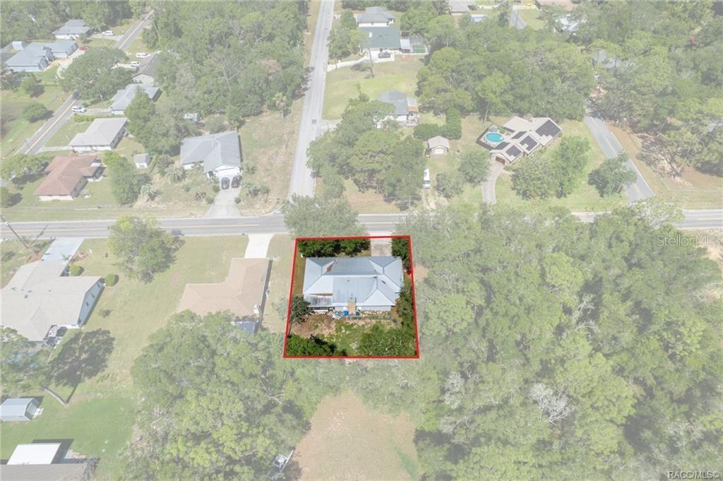 An aerial view shows a single-story house with a metal roof on a wooded lot — 1140 S HIGHLANDS AVENUE, INVERNESS, FL