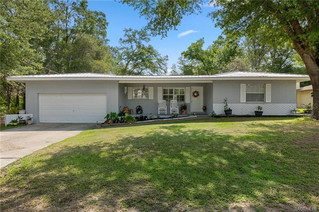 A single-story gray house with a white garage door, metal roof, and front lawn — 1140 S HIGHLANDS AVENUE, INVERNESS, FL