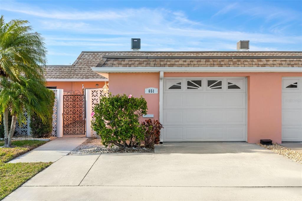 A peach-colored house exterior features a white garage door, a decorative metal gate, and landscaping — 651 BOCA CIEGA POINT BOULEVARD S, ST PETERSBURG, FL
