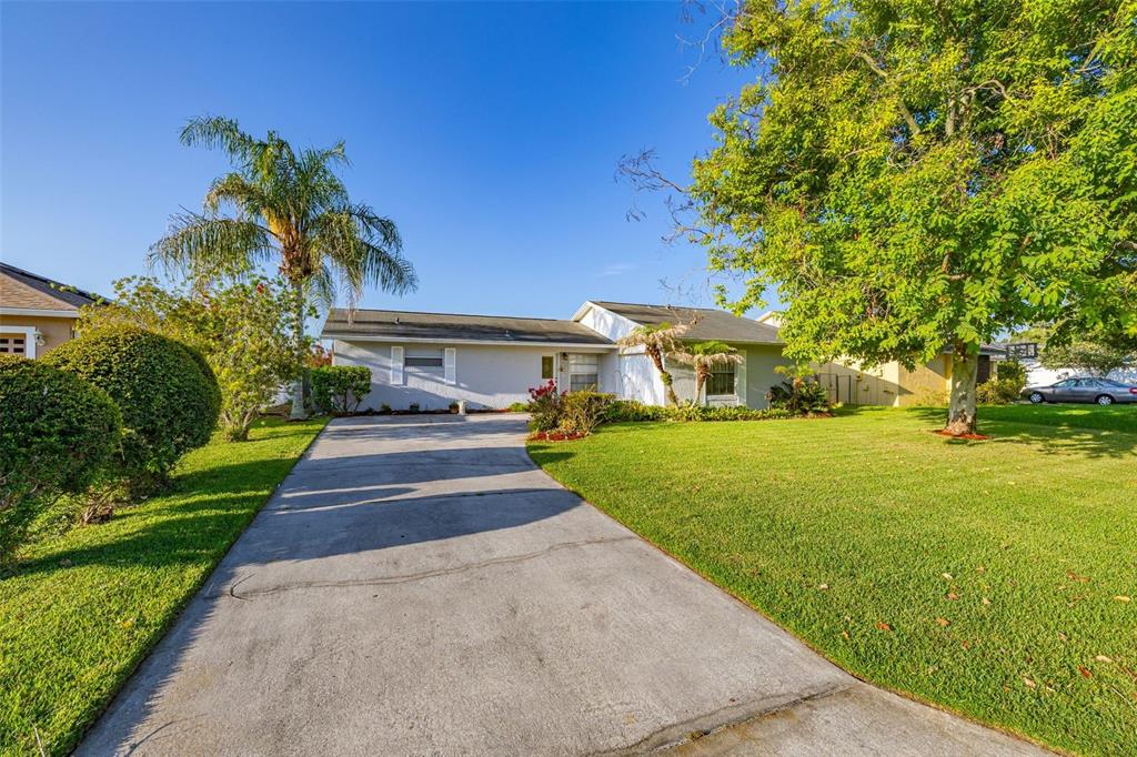 A single-story house with a concrete driveway, a large front lawn, and mature trees — 708 WEDGE LANE, POINCIANA, FL