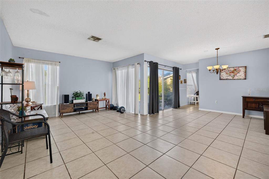 A spacious living area features light blue walls, tile flooring, and sliding glass patio doors — 708 WEDGE LANE, POINCIANA, FL