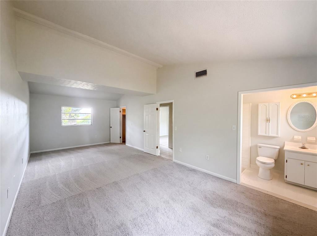 A bedroom with gray carpeting, a vaulted ceiling, and an attached bathroom with a vanity — 1870 N SEMINOLE ROAD, AVON PARK, FL