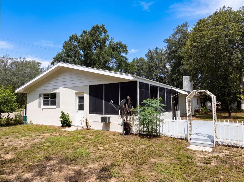 The exterior of a white house features a screened-in porch and a small fenced patio — 1870 N SEMINOLE ROAD, AVON PARK, FL