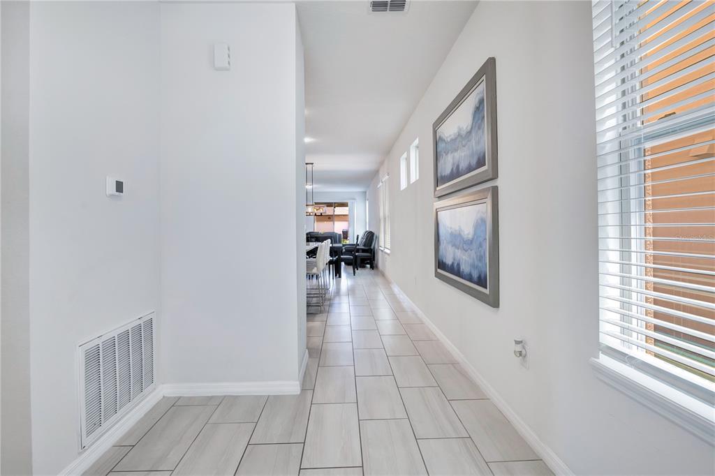 A long hallway with light tile flooring leads toward an open-concept living and dining area — 16802 OAKBORO STREET, WINTER GARDEN, FL