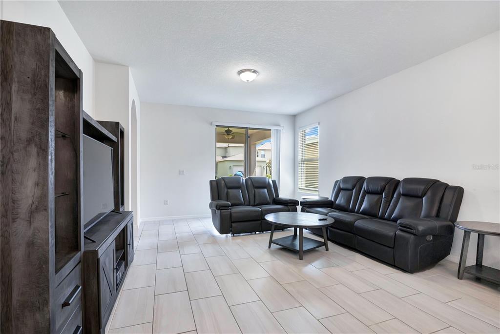 A living room features light tile flooring, white walls, a dark entertainment center, and leather furniture — 16802 OAKBORO STREET, WINTER GARDEN, FL
