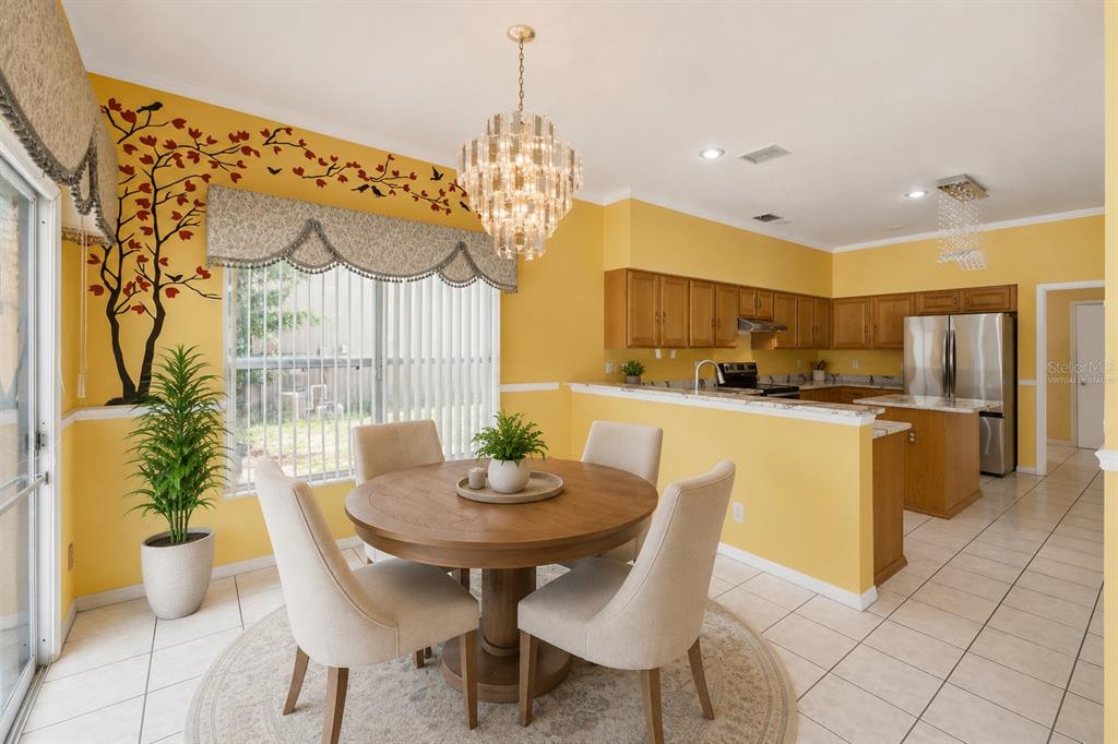 A dining area with a round wooden table, four chairs, and a yellow-walled kitchen — 6415 ABBEYDALE COURT, ORLANDO, FL