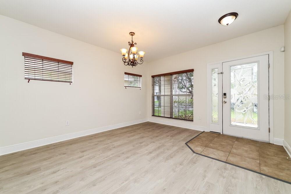 An empty dining room features light wood-look flooring, a chandelier, and a glass-paneled front door — 209 FERN GULLEY DRIVE, SEFFNER, FL