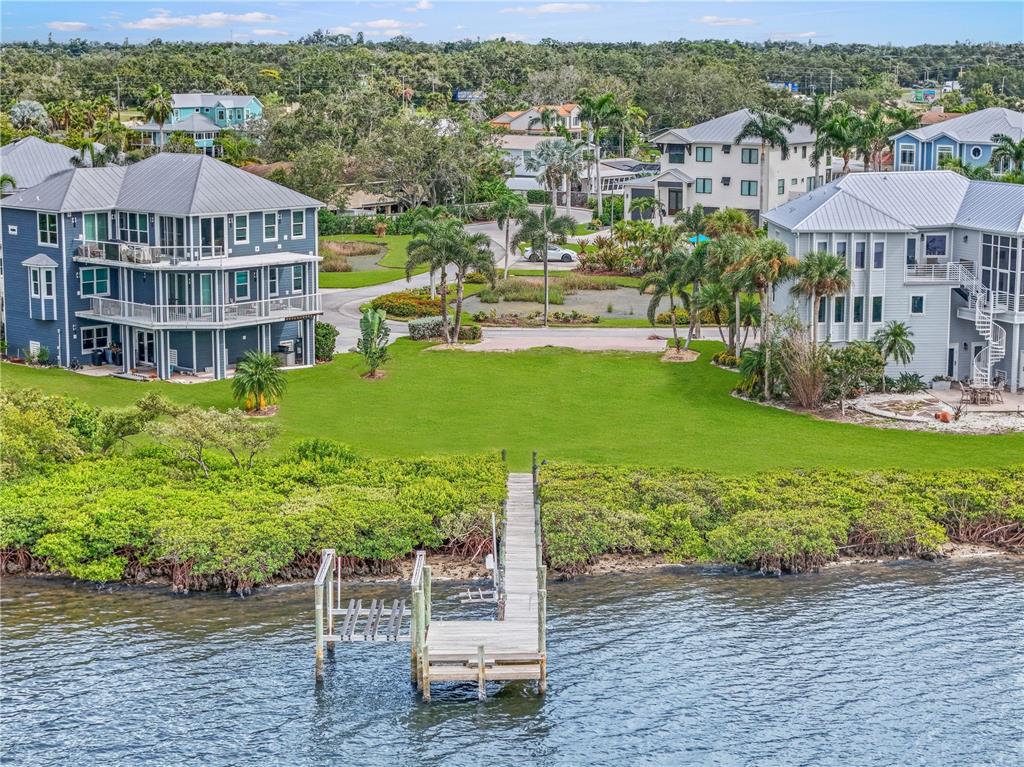 An elevated three-story house with a metal roof stands between two homes near water — 5539 2ND AVENUE CIRCLE W, PALMETTO, FL