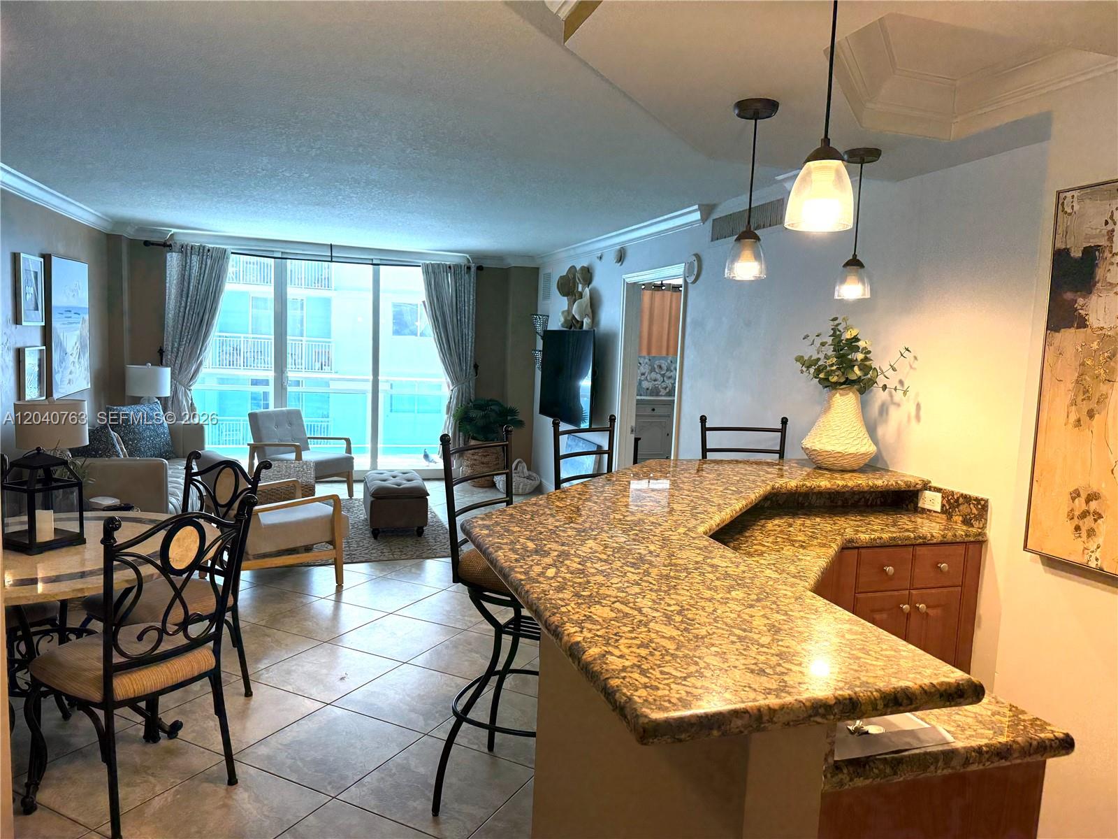 An open-concept living and dining area features a granite breakfast bar and tile flooring — 6917 Collins Ave # 506, Miami Beach FL 33141, MIAMI BEACH, FL