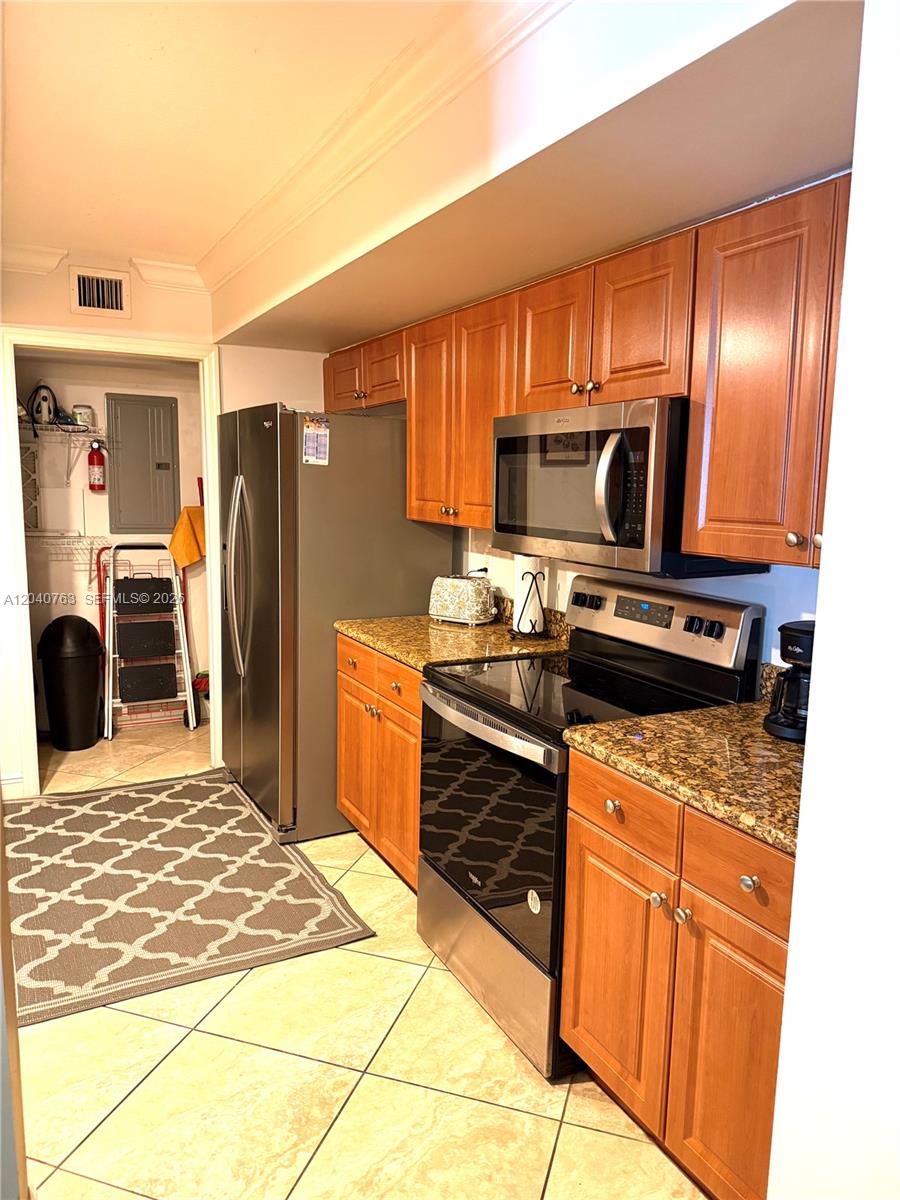 A kitchen with wood cabinets, granite countertops, stainless steel appliances, and tile flooring — 6917 Collins Ave # 506, Miami Beach FL 33141, MIAMI BEACH, FL