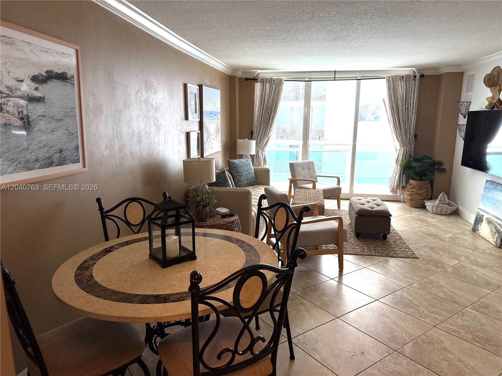 A living and dining area features tile floors, neutral walls, and a balcony view — 6917 Collins Ave # 506, Miami Beach FL 33141, MIAMI BEACH, FL