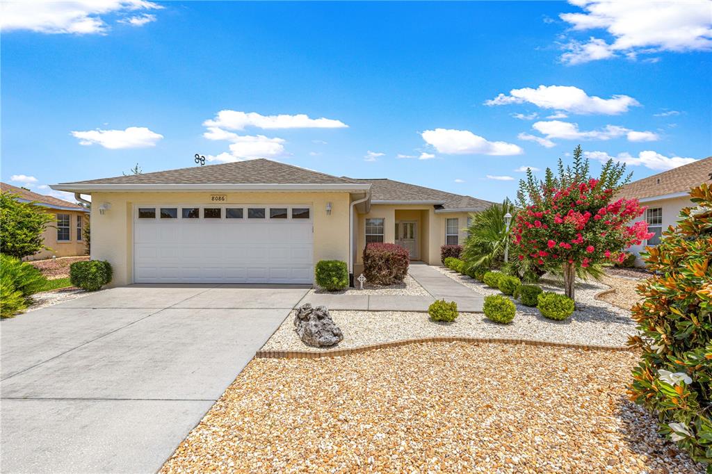 A single-story house with a white garage door, tan stucco siding, and a gravel front yard — 8086 SW 81ST LOOP, OCALA, FL