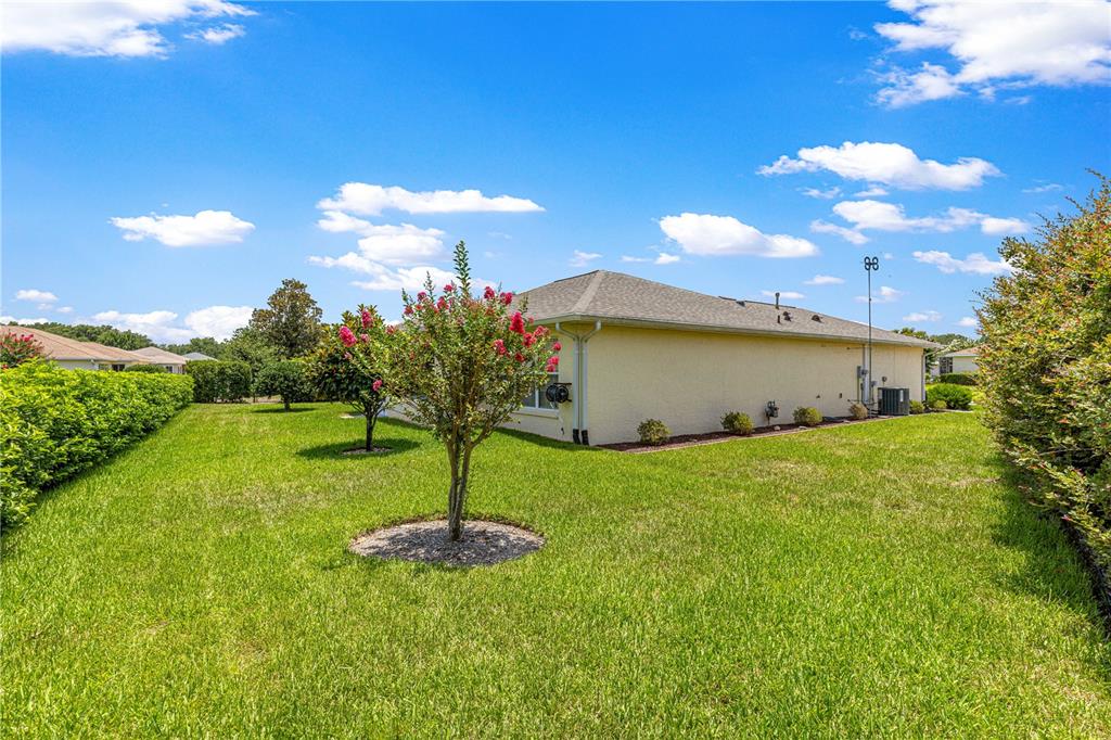 A side view of a beige house with a grassy yard and flowering trees — 8086 SW 81ST LOOP, OCALA, FL