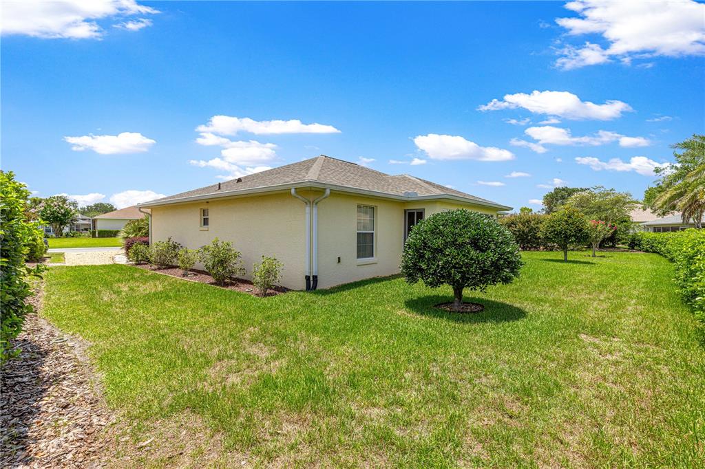 The exterior of a beige single-story house features a hip roof and a grassy backyard — 8086 SW 81ST LOOP, OCALA, FL