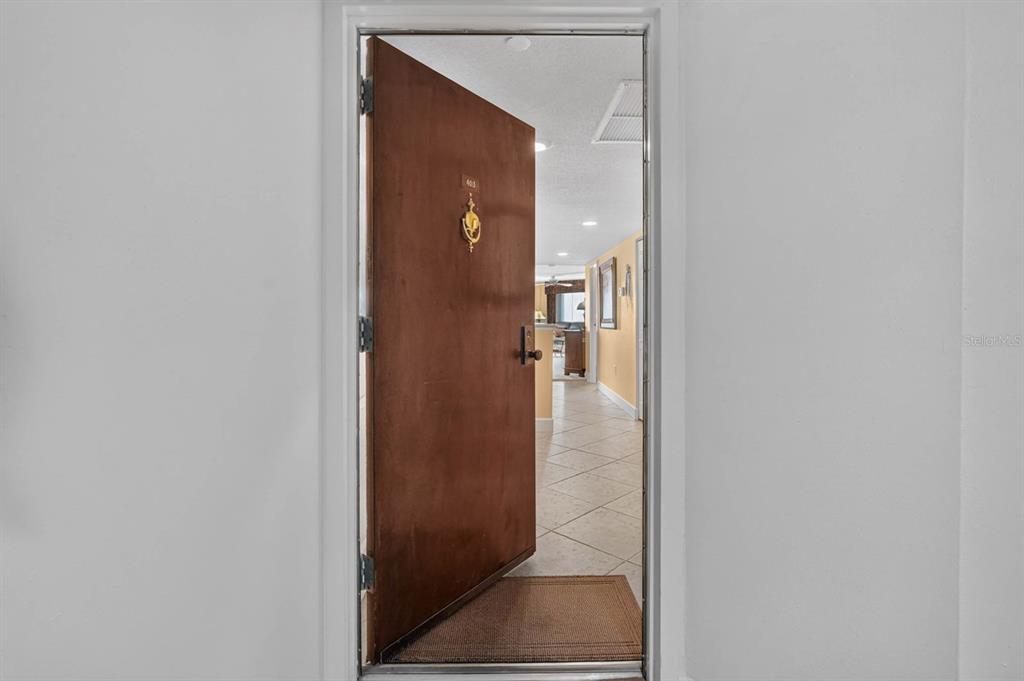 An open wooden door reveals a tiled entryway leading into a brightly lit interior space — 925 N HALIFAX AVENUE UNIT 403, DAYTONA BEACH, FL