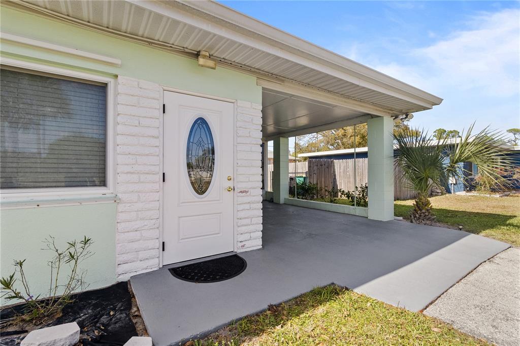 A white front door with an oval glass insert sits beside a covered concrete carport — 4419 MELBOURNE STREET, PUNTA GORDA, FL