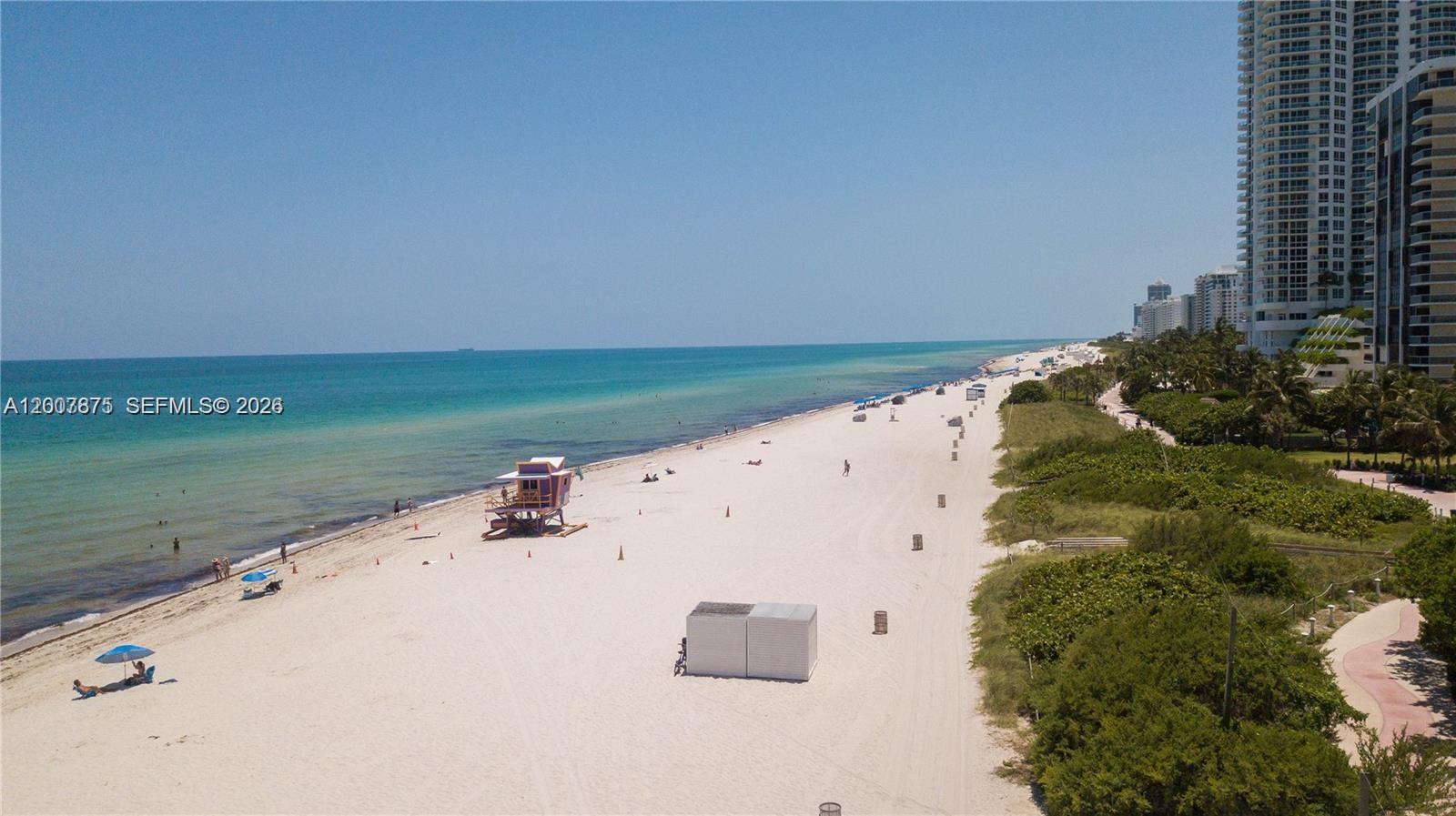 An aerial view shows a sandy beach with a lifeguard tower and high-rise buildings — 6515 Collins Ave # 1609, Miami Beach FL 33141, MIAMI BEACH, FL