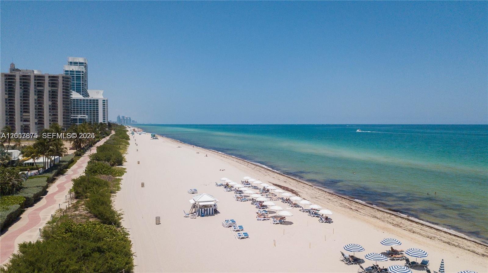 An aerial view shows a sandy beach with rows of umbrellas and tall buildings nearby — 6515 Collins Ave # 1609, Miami Beach FL 33141, MIAMI BEACH, FL