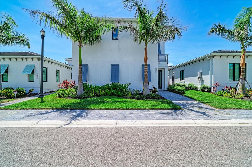 A two-story white house with blue shutters and palm trees stands behind a paved walkway — 5935 CAT CLAW LANE, BRADENTON, FL