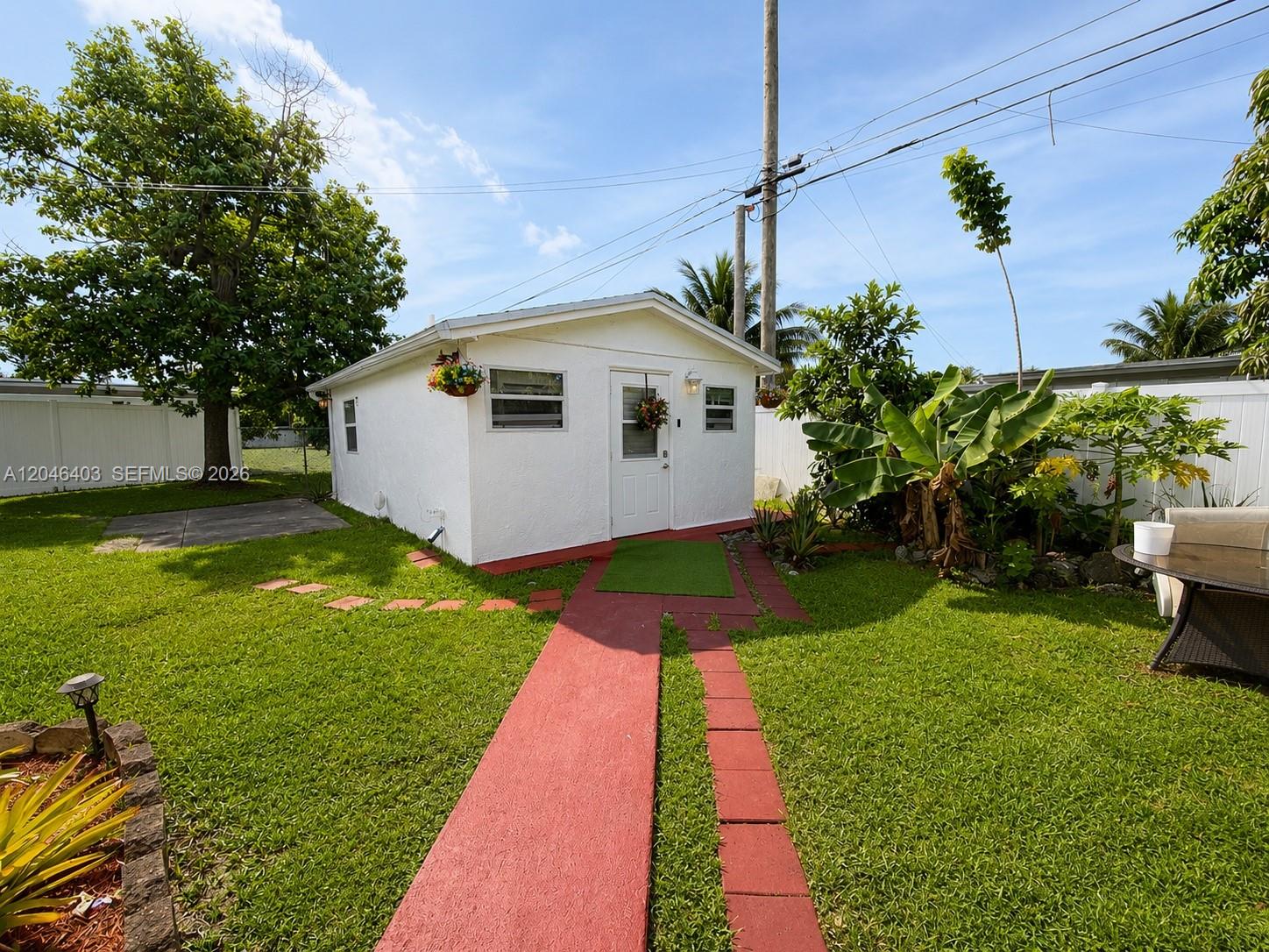 A small white detached structure sits in a grassy backyard with a red walkway — 6118 Mayo St # 3, Hollywood FL 33023, HOLLYWOOD, FL