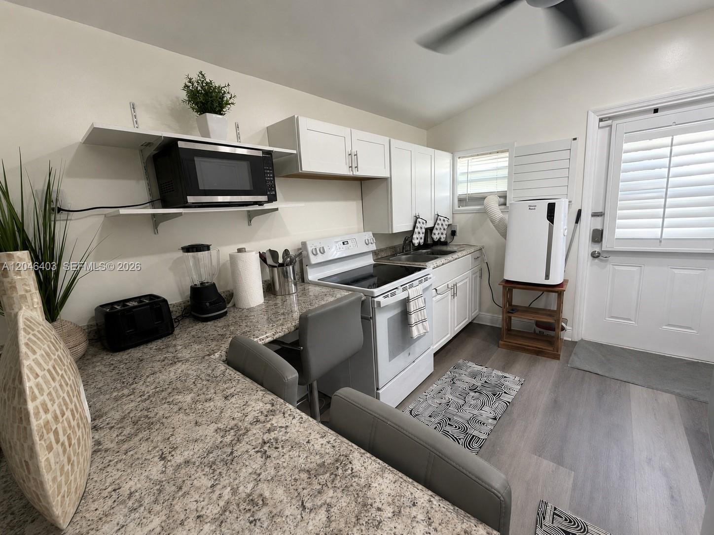 A kitchen features white cabinets, granite countertops, a stove, and a portable air conditioner — 6118 Mayo St # 3, Hollywood FL 33023, HOLLYWOOD, FL