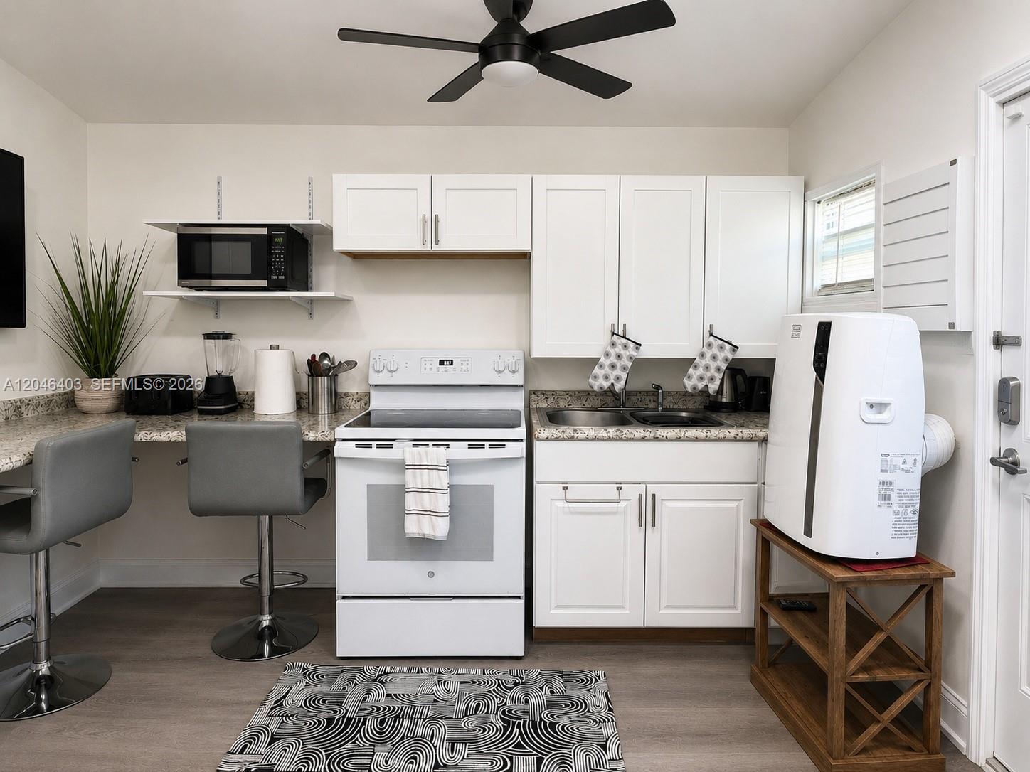 A small kitchen features white cabinets, a white stove, granite countertops, and a portable air conditioner — 6118 Mayo St # 3, Hollywood FL 33023, HOLLYWOOD, FL