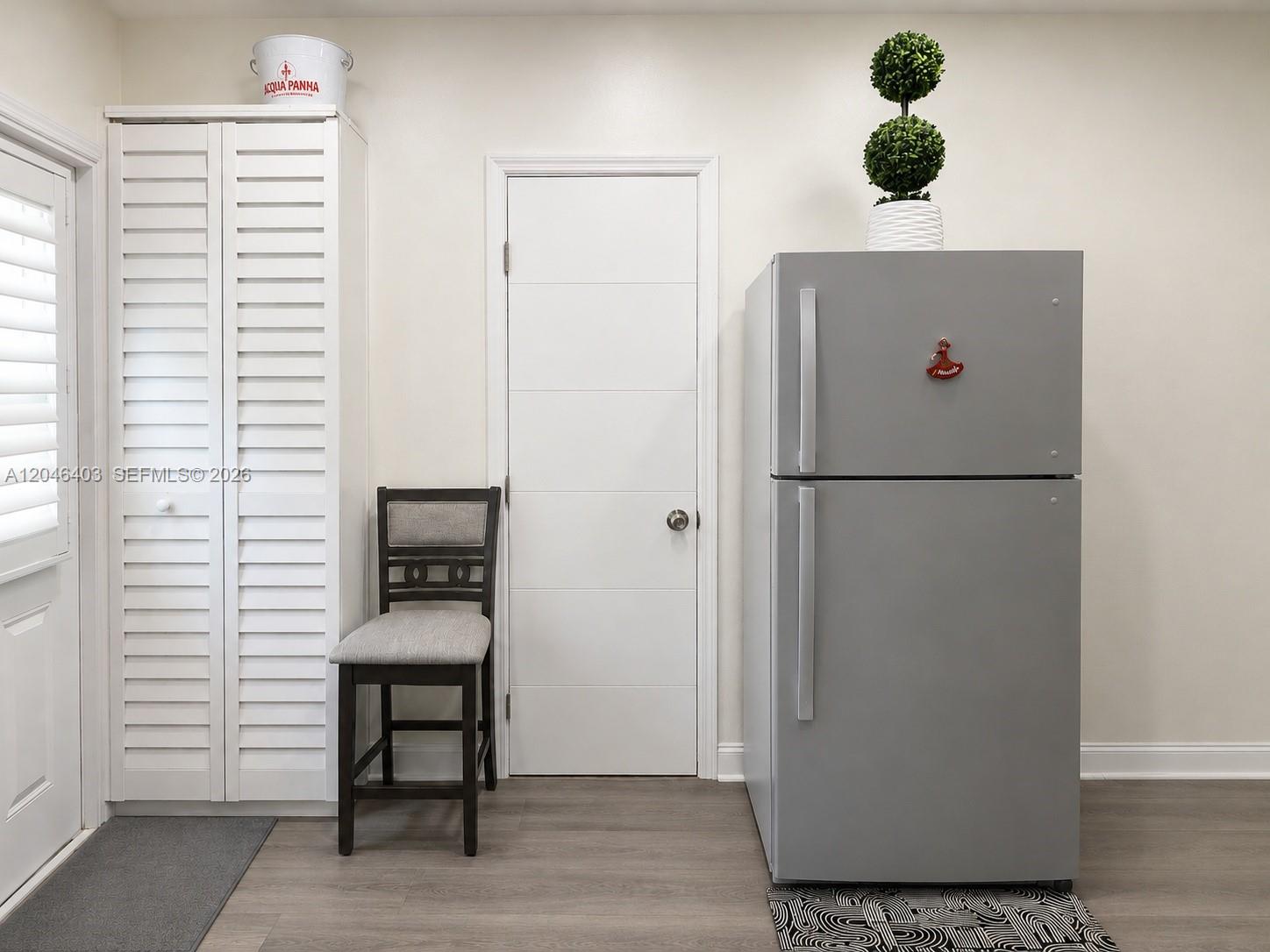 A room features a gray refrigerator, a wooden chair, a white door, and louvered cabinets — 6118 Mayo St # 3, Hollywood FL 33023, HOLLYWOOD, FL