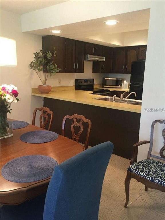 A dining area with a wooden table leads into a kitchen with dark cabinets — 328 MARINER DRIVE UNIT 328, TARPON SPRINGS, FL