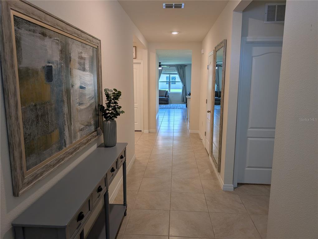 A hallway with tile flooring leads toward a living area with a window and curtains — 3329 EASTGROVE TERRACE, SANFORD, FL