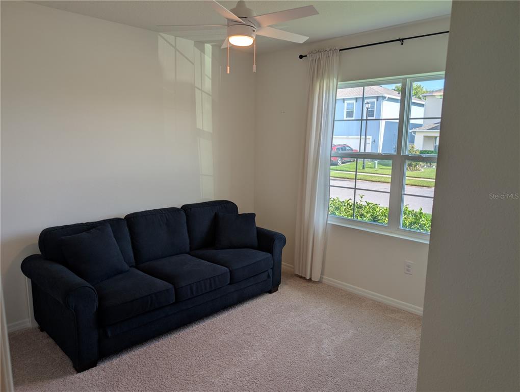A room with beige carpet, a dark blue sofa, and a window with white curtains — 3329 EASTGROVE TERRACE, SANFORD, FL