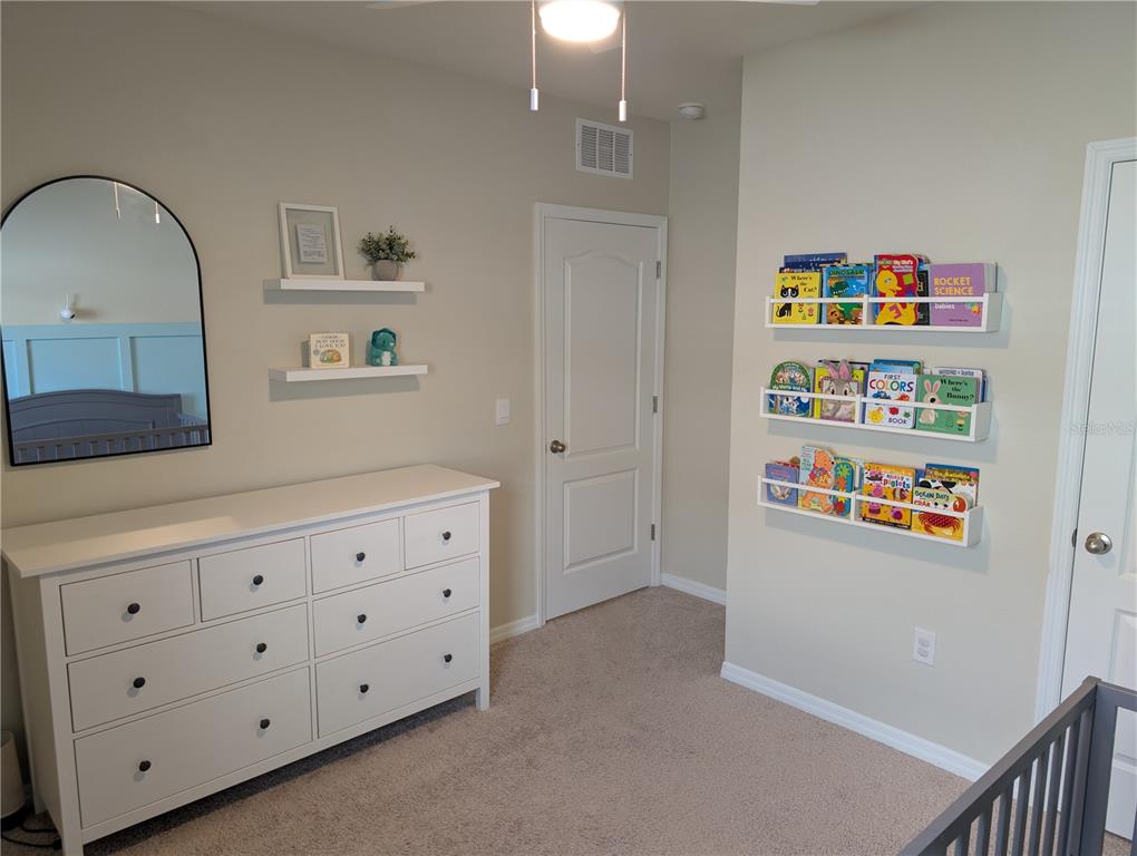 A nursery features a white dresser, wall-mounted bookshelves, and an arched mirror on a beige wall — 3329 EASTGROVE TERRACE, SANFORD, FL