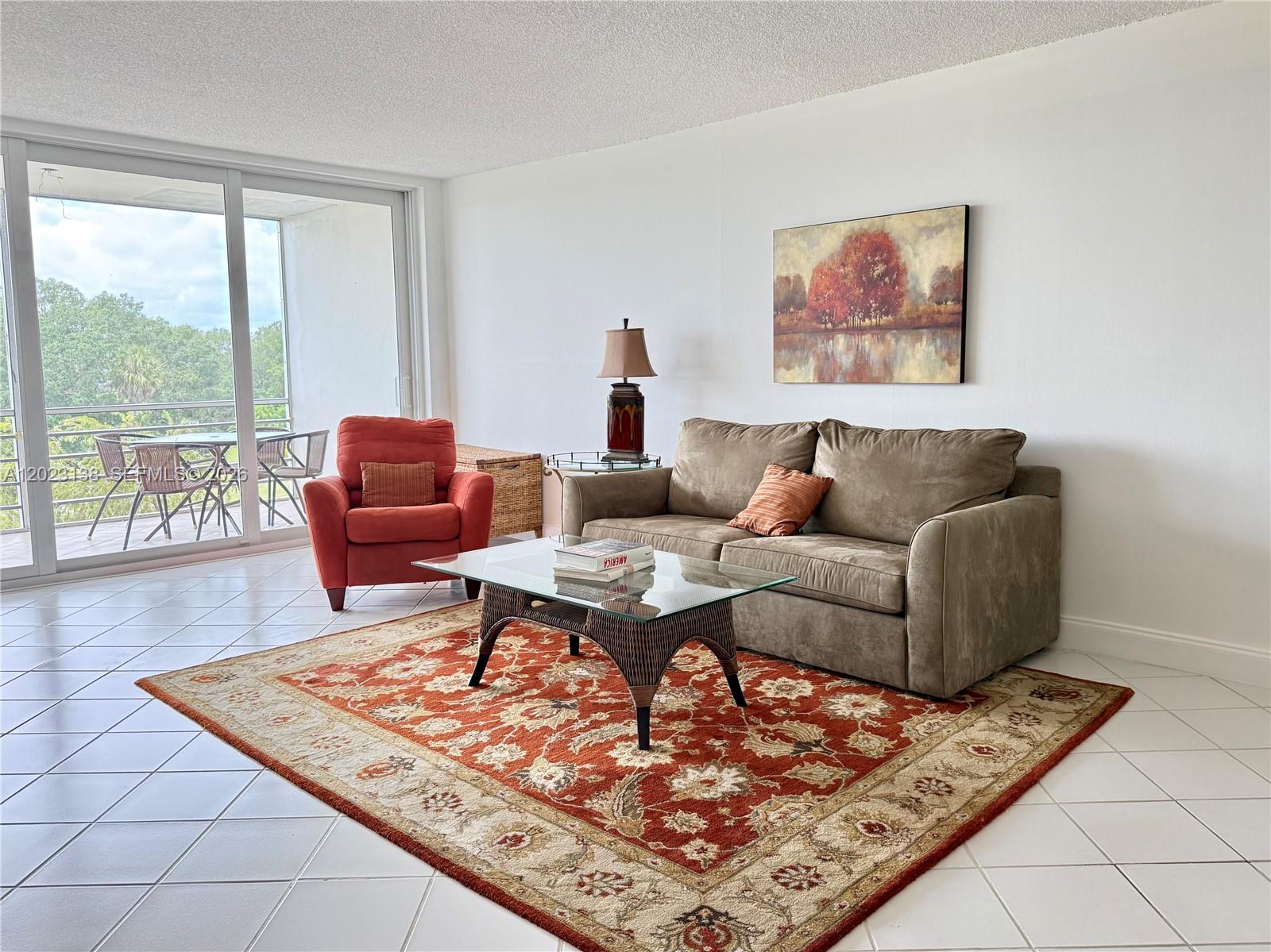 A living room features a brown sofa, orange armchair, glass coffee table, and patterned rug — 2671 S Course Dr # 408, Pompano Beach FL 33069, POMPANO BEACH, FL