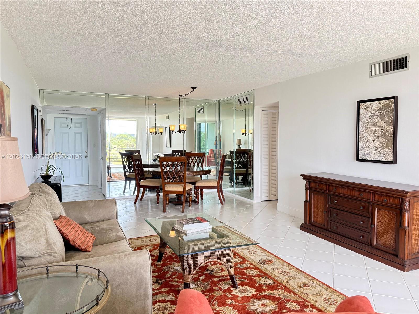 A living and dining area features a mirrored wall, tile flooring, and a red rug — 2671 S Course Dr # 408, Pompano Beach FL 33069, POMPANO BEACH, FL