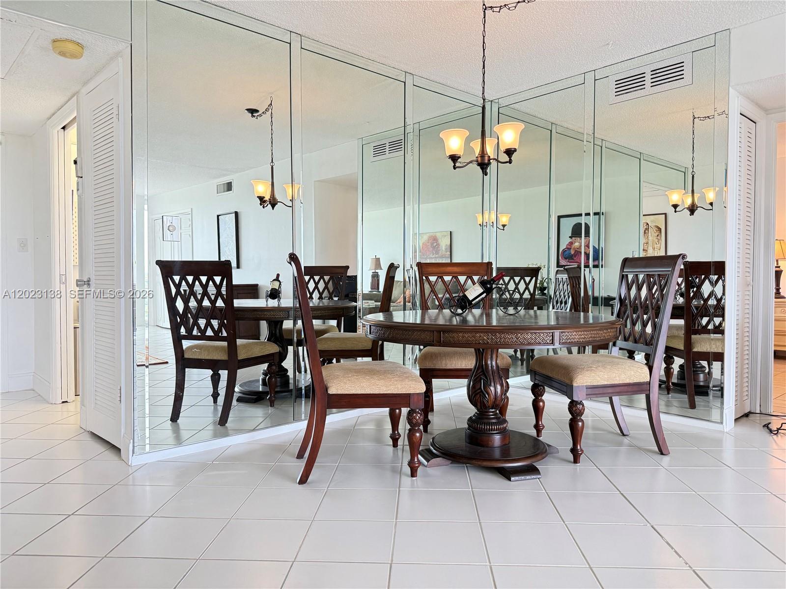 A dining area features a round wooden table, four chairs, and a mirrored accent wall — 2671 S Course Dr # 408, Pompano Beach FL 33069, POMPANO BEACH, FL