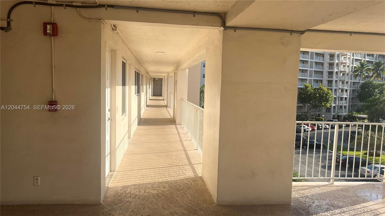 An outdoor apartment building walkway features a concrete floor, white railings, and exterior doors — 2901 S Palm Aire Dr # 408, Pompano Beach FL 33069, POMPANO BEACH, FL