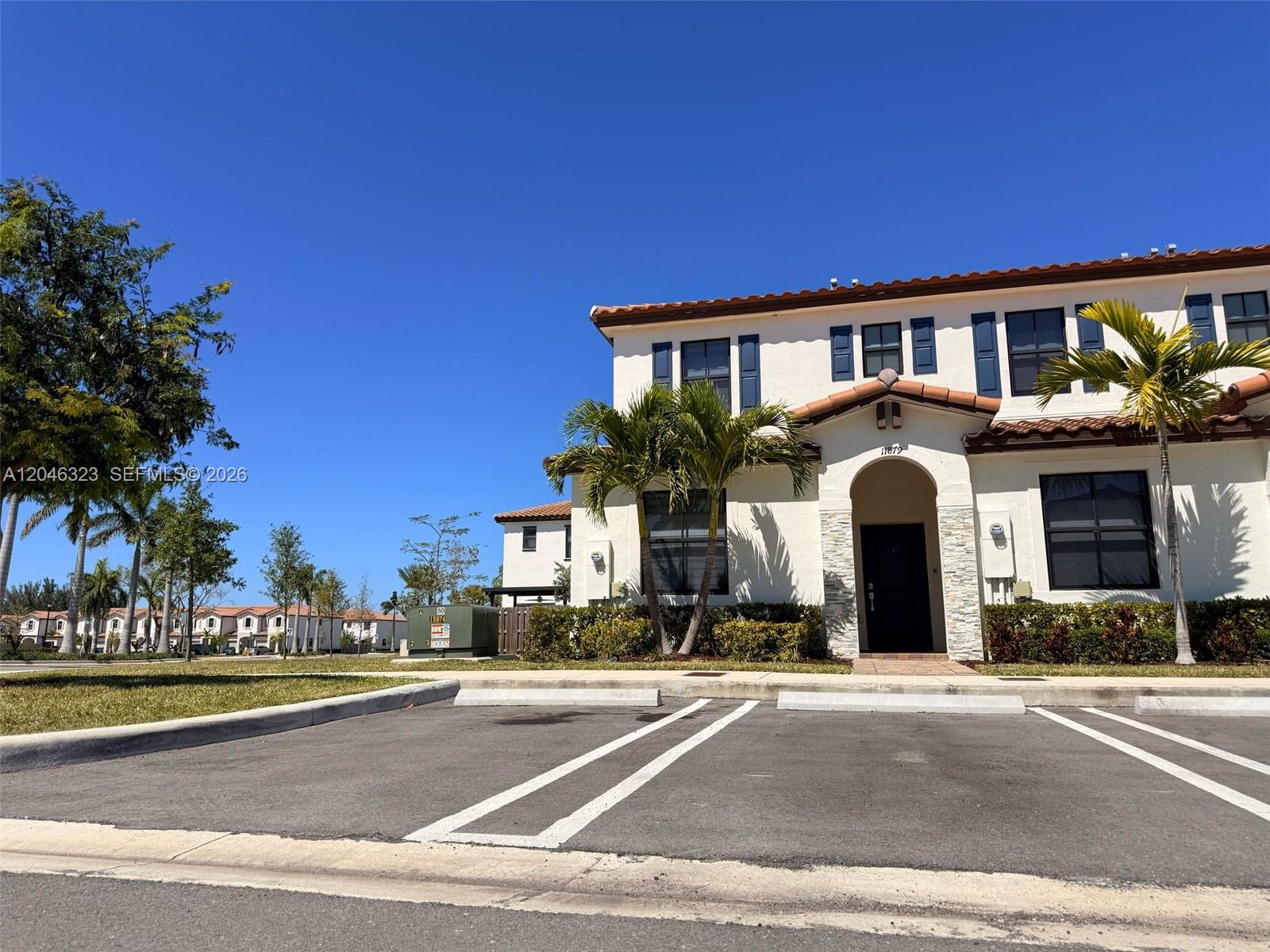 A two-story stucco townhouse with a tiled roof and palm trees in front — HOMESTEAD, FL