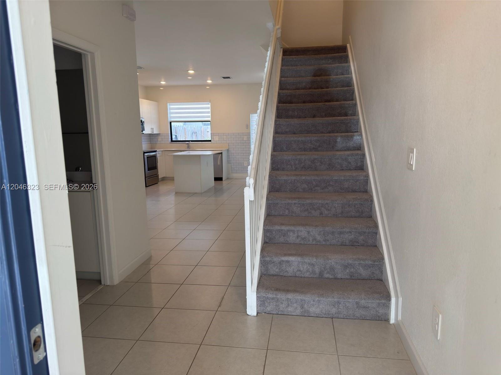 A tiled entryway leads to a carpeted staircase and an open-concept kitchen with white cabinets — HOMESTEAD, FL