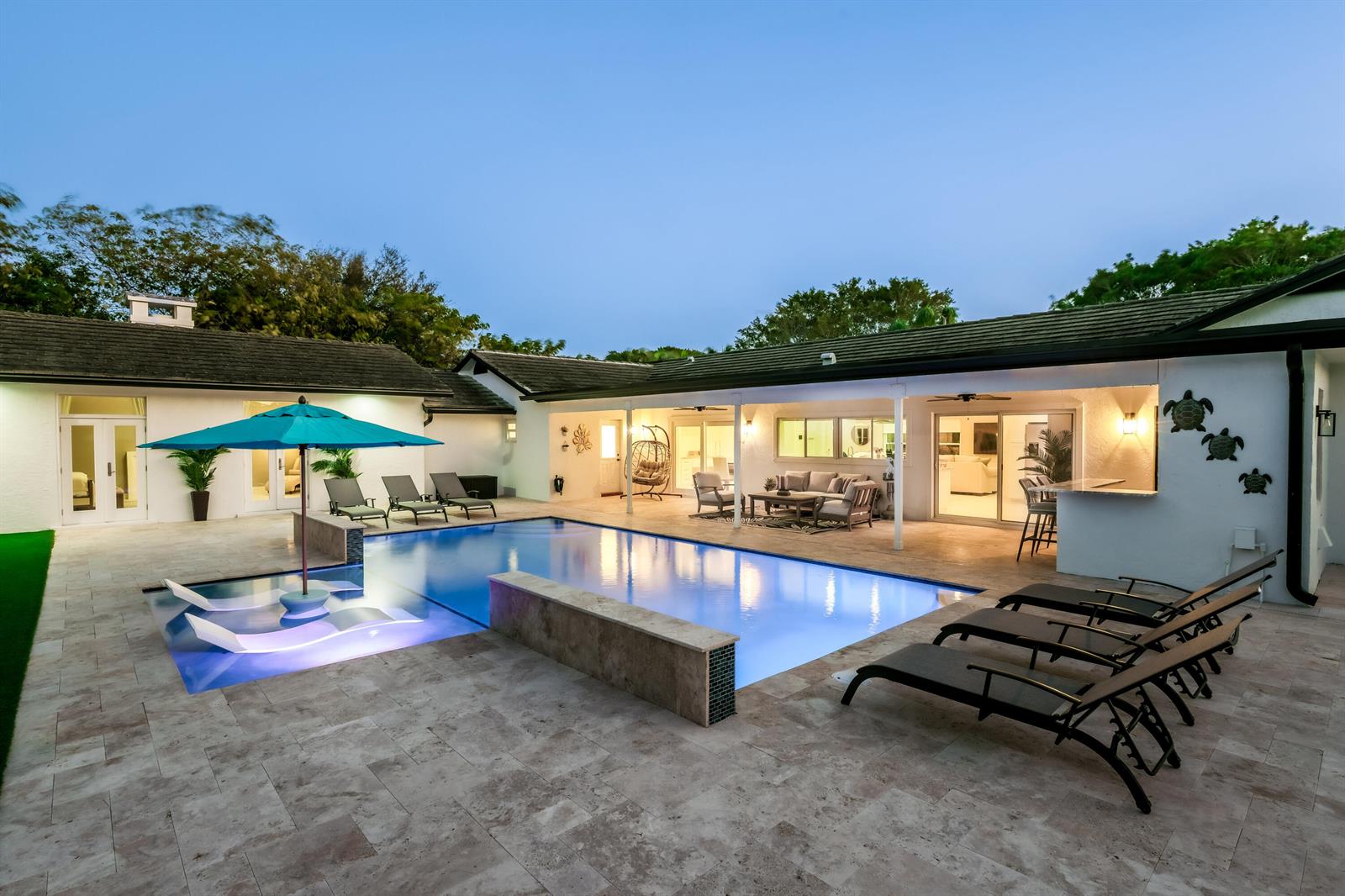 A backyard features a swimming pool with a sun shelf, lounge chairs, and a covered patio — 3127 Sherwood Boulevard, Delray Beach FL 33445, DELRAY BEACH, FL