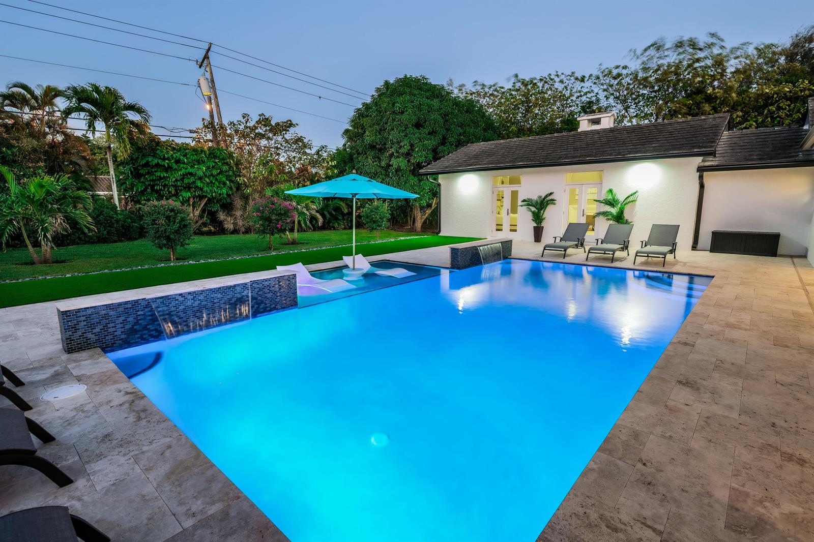 A backyard swimming pool with a water feature, lounge chairs, and a patio at dusk — 3127 Sherwood Boulevard, Delray Beach FL 33445, DELRAY BEACH, FL