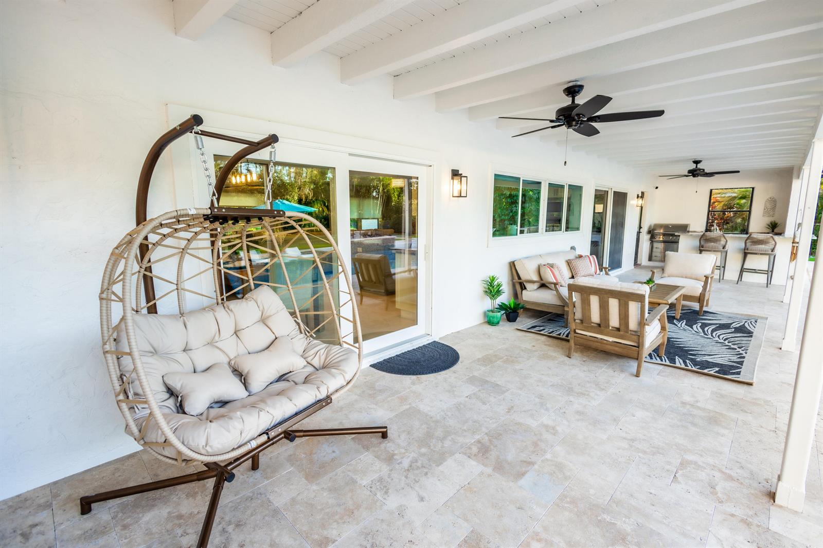 A covered patio features a hanging egg chair, outdoor seating, and a built-in bar area — 3127 Sherwood Boulevard, Delray Beach FL 33445, DELRAY BEACH, FL