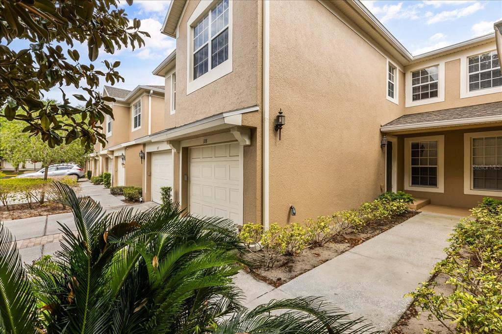 A tan two-story townhouse with a garage, concrete walkway, and small front yard landscaping — 6440 AXEITOS TERRACE UNIT 108, ORLANDO, FL