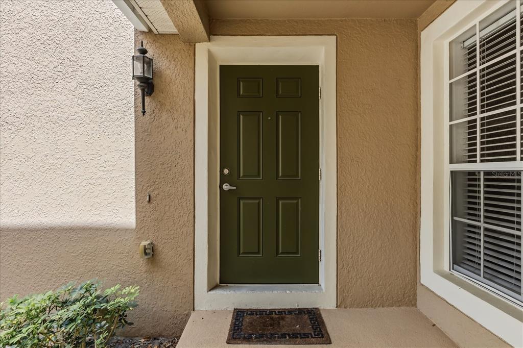 A dark green front door with a small welcome mat sits on a covered porch — 6440 AXEITOS TERRACE UNIT 108, ORLANDO, FL