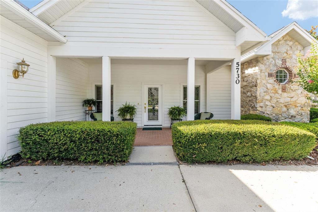 A white house exterior features a covered front porch, brick walkway, and manicured green hedges — 5730 NW 52ND PLACE, GAINESVILLE, FL