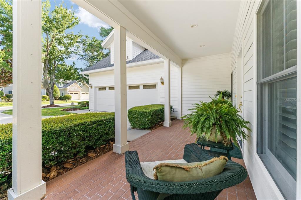 A covered brick porch features a wicker chair, a potted fern, and white columns — 5730 NW 52ND PLACE, GAINESVILLE, FL