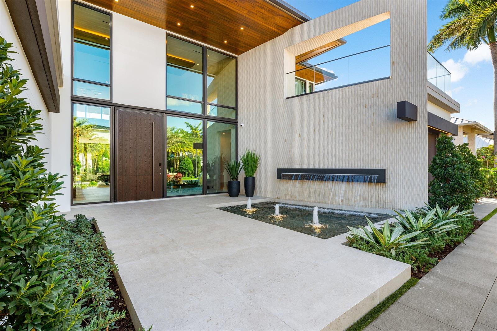 The exterior of a modern home features a large wooden door, glass windows, and a fountain — 234 W Alexander Palm Road, Boca Raton FL 33432, BOCA RATON, FL