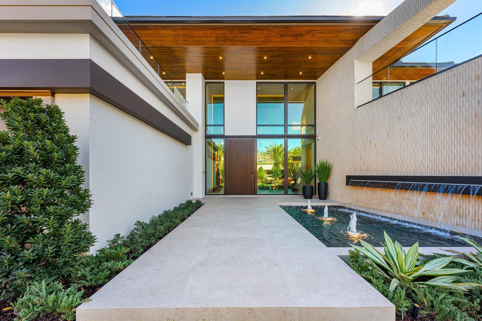 A modern home entrance features a stone walkway, a water feature, and a glass-paneled door — 234 W Alexander Palm Road, Boca Raton FL 33432, BOCA RATON, FL