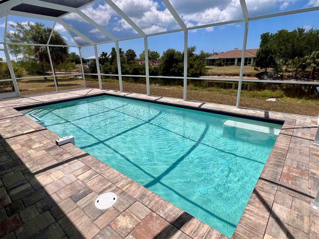 A screened-in swimming pool with paver decking overlooks a pond and neighboring houses — 55 ROTONDA CIRCLE, ROTONDA WEST, FL